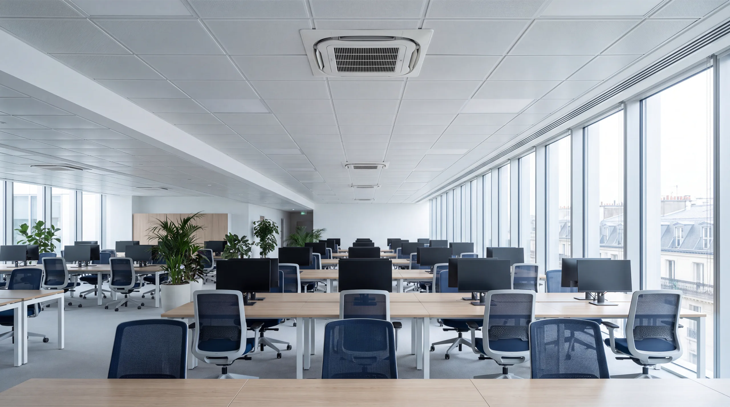 Plateau de bureaux en open space, vide, équipé de cassettes de climatisation encastrées au plafond, avec vue sur les toits parisiens.